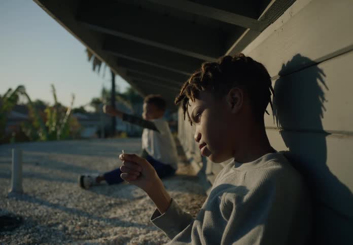 Two brothers sit on gravel against building under overhang and examine piece
