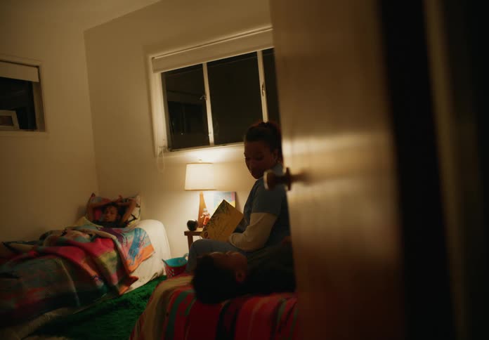 Mother reads book to children lying in bed at night