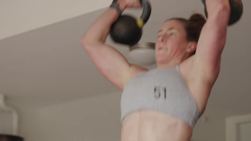 A woman is lifting weights while standing indoors