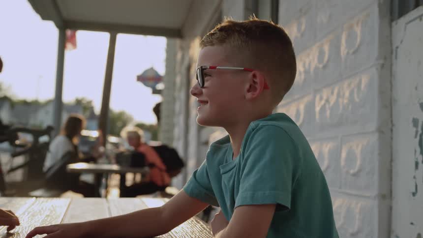 A boy laughs while sitting on a restaurant patio with his grandfather