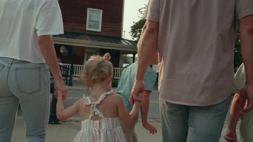 A mother and father hold their daughters hands as they walk with their sons along a suburban street