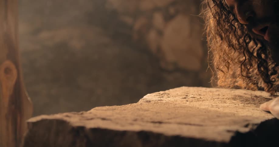 A man with curly hair wipes dust from the top of a large piece of stone