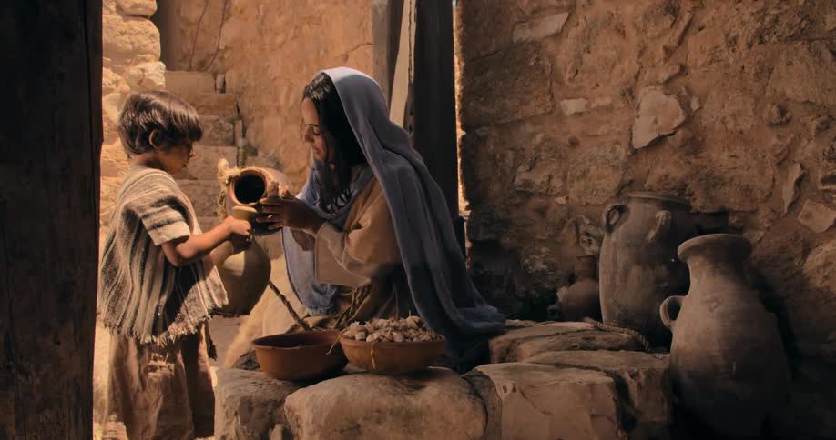 A woman pouring water from a pitcher into a little boys pitcher in an alley way