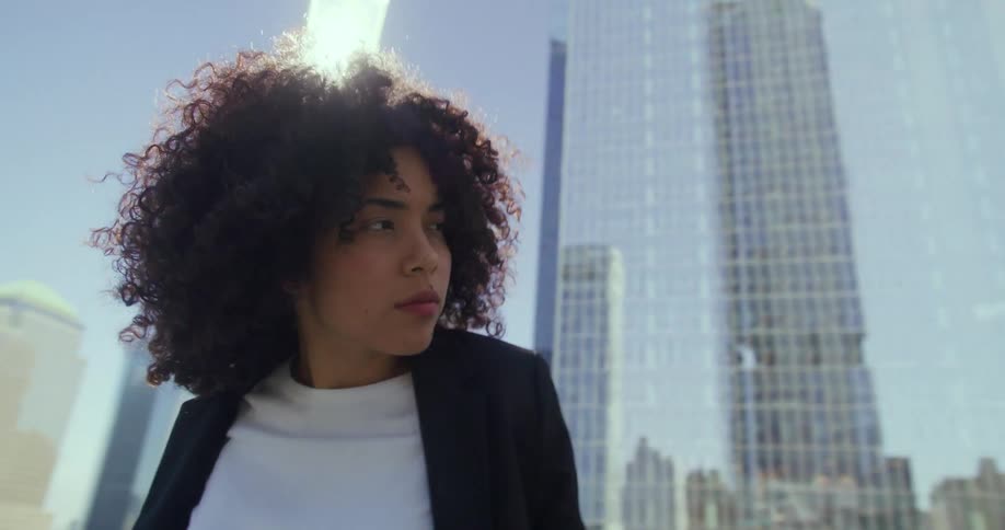 Woman leans against rail while standing outdoors near skyscrapers on bright sunny day