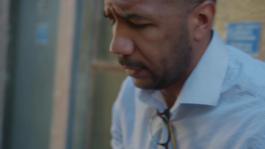 A man is standing next to a building talking on his cell phone and he finishes and looks up at the sky