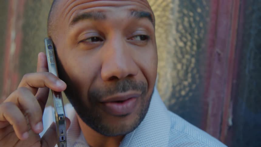 A man is standing near a building talking on his cell phone