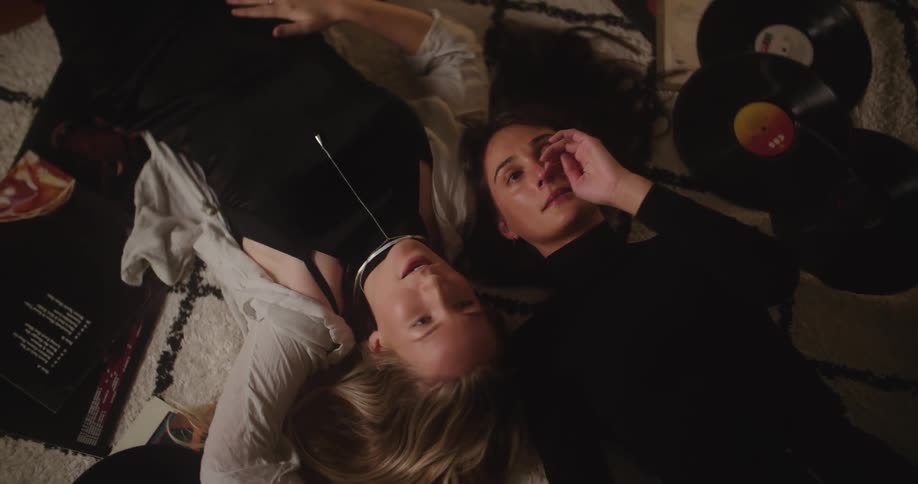 Two women lying on the floor listening to records and talking at nighttime