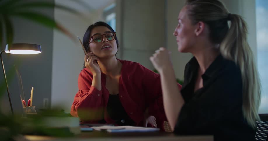 Two women sit at desk with a laptop and hold a discussion