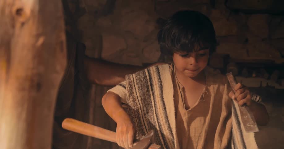 A young boy uses a hammer and chisel on a piece of stone