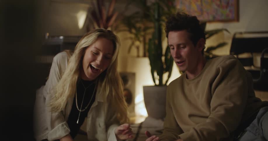 Blonde woman and man laughing and talking while hanging out in living room