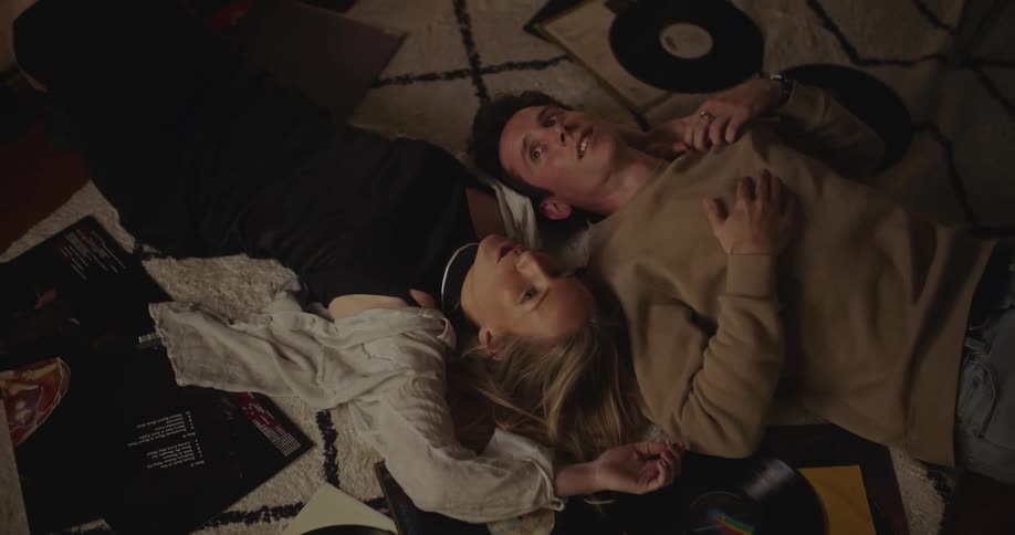 A man and a woman are laying on the floor surrounded by records and talking