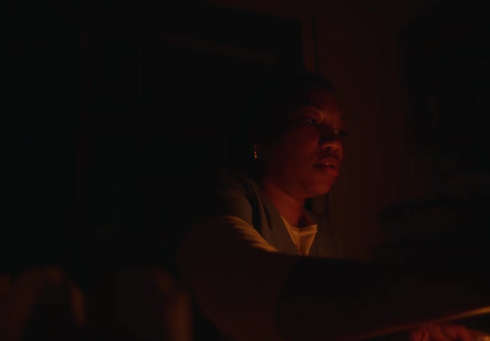 A woman sitting at a table lights a match and lights candles in the dark