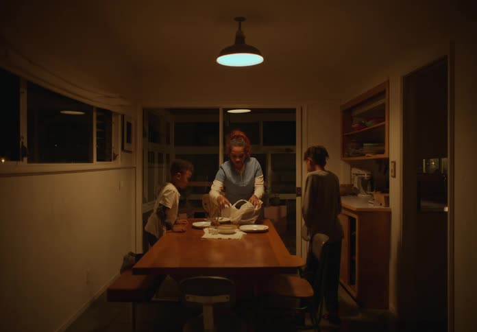 After entering the dining room at night mother puts takeout on the table and then sits to say grace with her sons