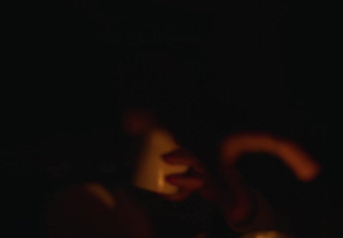Woman lights candle in dark room as youth stands next to her then she serves from takeout container