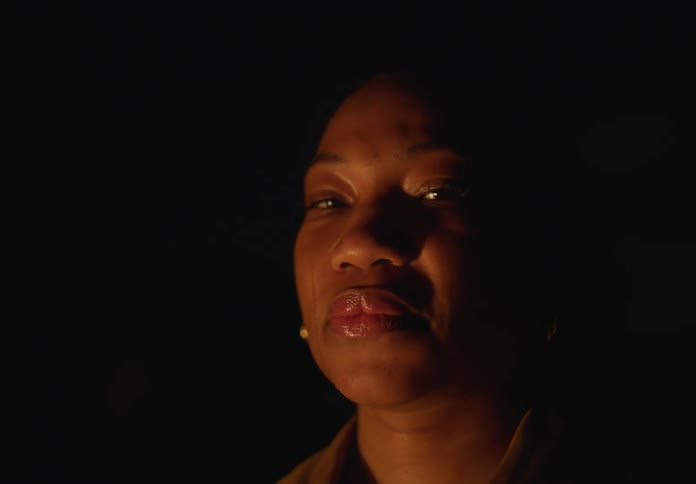 A woman stands in the darkness and wipes tears from her eyes