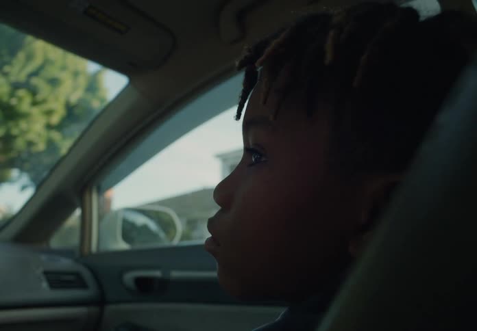 A young boy is sitting in the passenger seat of an automobile as it travels through a neighborhood