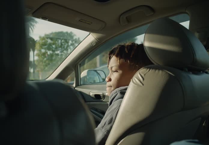 A young boy is sitting in the passenger seat of an automobile as it travels through a neighborhood