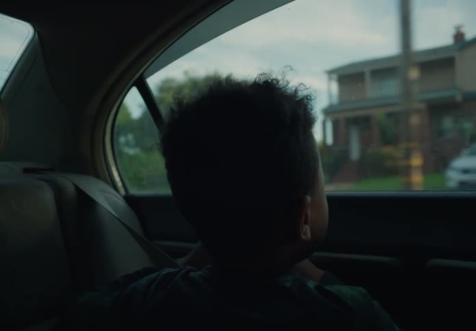 Boy on the backseat of a driving car looking at the houses of a small town trough the window