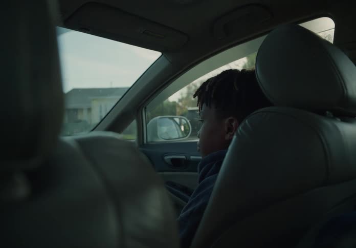 A young boy is sitting in the passenger seat of an automobile as it travels through a neighborhood