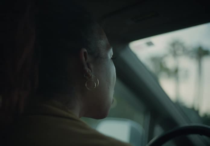 A woman is sitting behind the steering wheel of an automobile as she drives her car through a neighborhood
