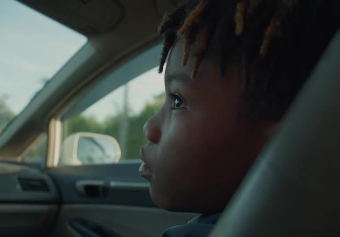 A young boy is sitting in the passenger seat of an automobile as it travels through a neighborhood