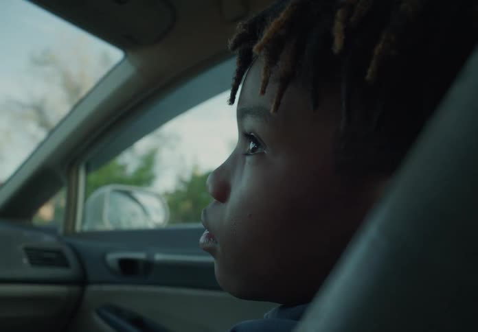 A young boy is sitting in the passenger seat of an automobile as they travel through a neighborhood