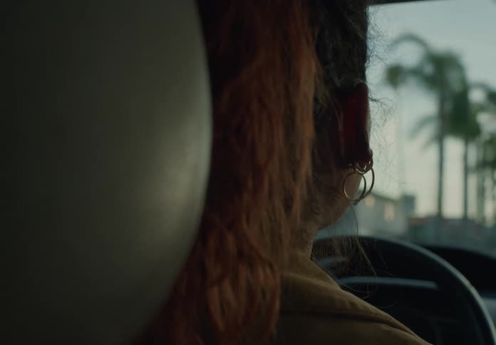 A close up of the back of a womans head as she drives her car down the road