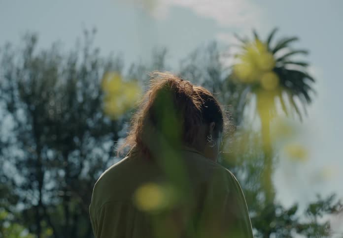 Back of the head of a woman standing outdoors feeling the morning sun on her face