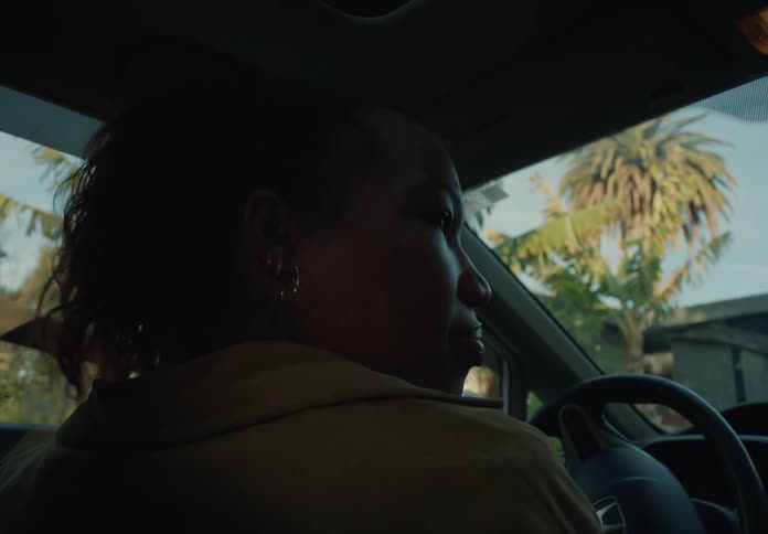 A woman is sitting behind the steering wheel of an automobile as she drives her car and gets out when she arrives at home