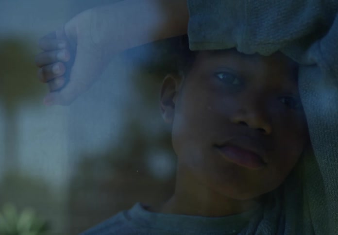 A boy standing in front of a glass window leaning against it looking out