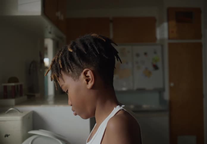 A boy standing washing dishes at the kitchen sink at home