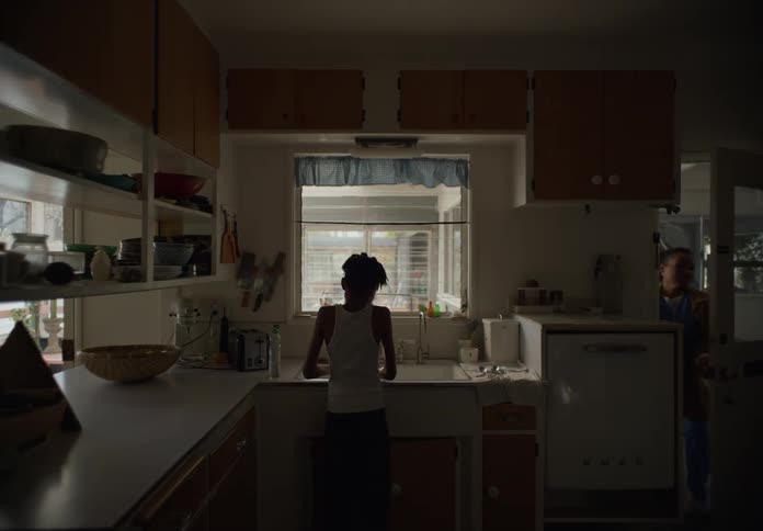 Boy with dreadlocks and white undershirt does the dishes in the kitchen