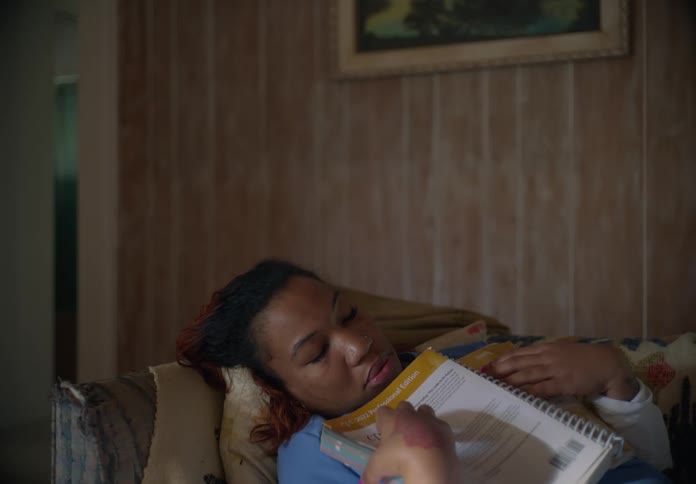 Woman wearing scrubs arrives home and sits down to read before falling asleep and then her son makes her comfortable