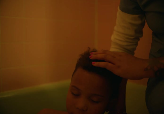 A parent caresses the hair of a young boy who is sitting in the bathtub