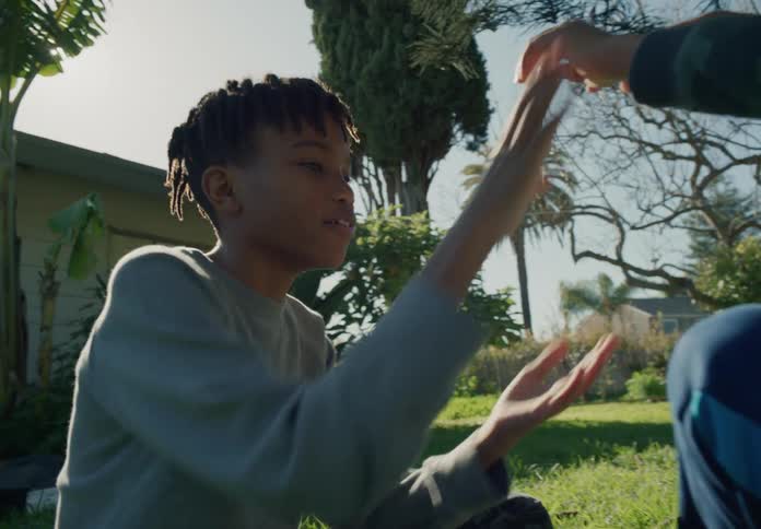 Two young brothers are sitting on the grass under a sunny sky playing rockpaperscissors