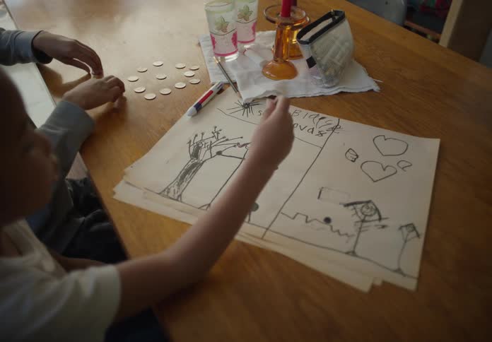 Boys sitting at the dining table at home playing with coins and drawing