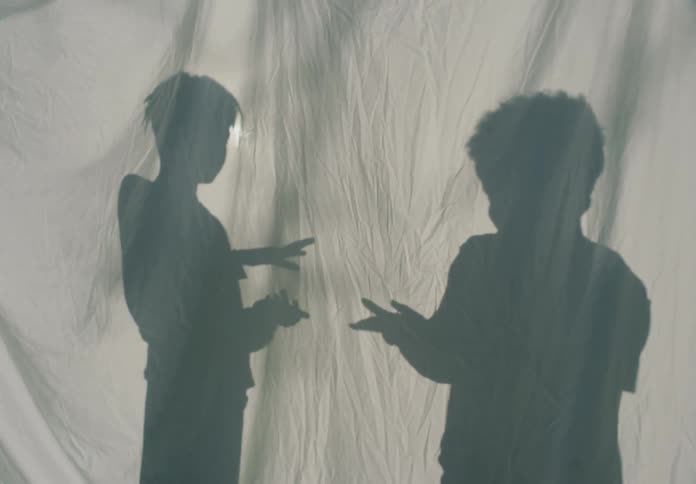 Silhouette of boys playing rock paper scissors behind a white sheet outdoors