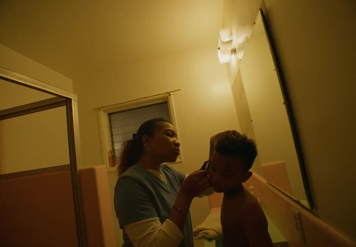 A female is shaving a black childs hair