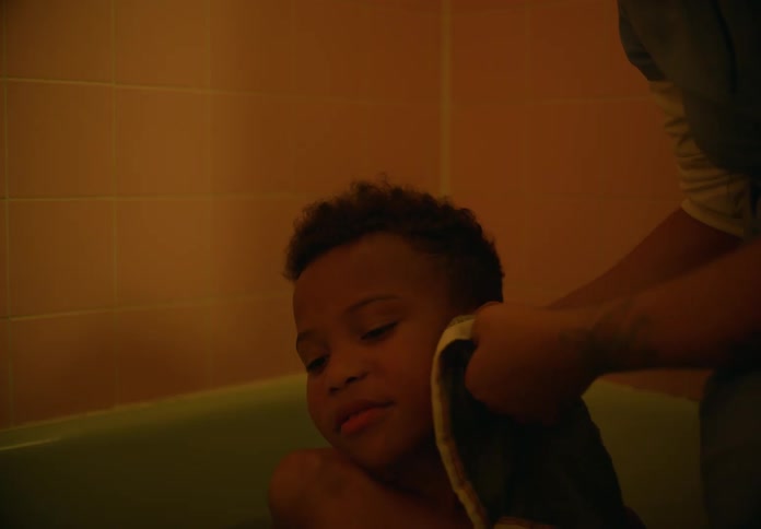 Mother washes face of her son with a washcloth as he sits in bathtub