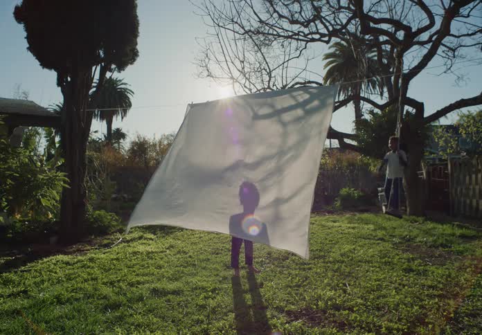 Boy projects his shadow on a white bed sheet drying in the backyard at morning