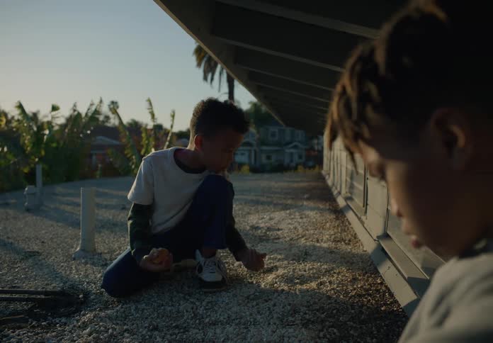 Brothers entertain themselves near building in residential neighborhood as the youngest eats fruit
