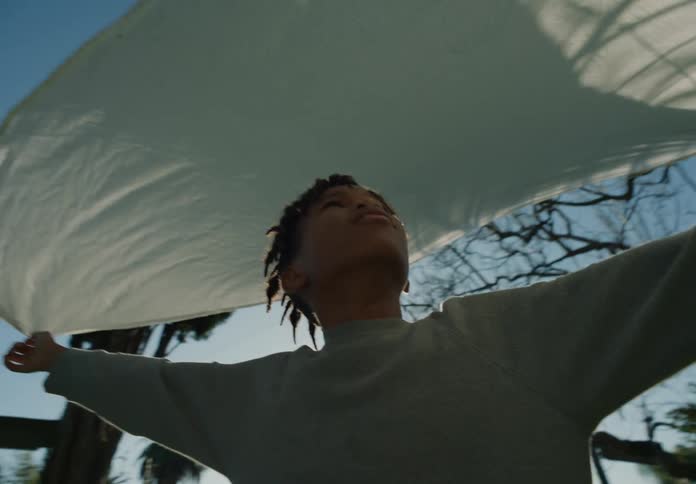 Youth briefly holds ends of sheet drying on clothesline in yard