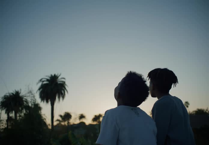 A pair of boys look at the distant sky while sitting together outdoors at sunset