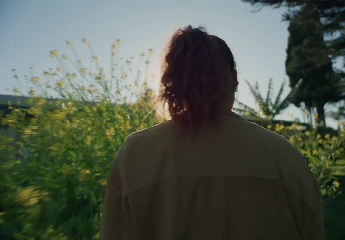 A woman walks through a yard full of a lot of vegetation growing in it