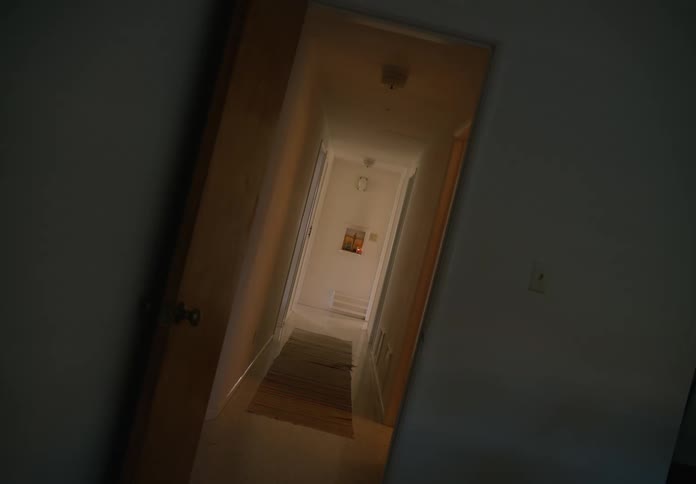 View of a hallway and the shelf on the wall at the end of the hallway shot from a room with the door open