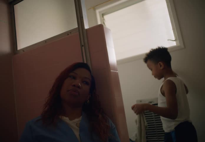 Boy with white undershirt walks by woman with red hair and blue shirt in the bathroom