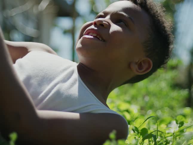 Two boys with white undershirts play with each other laughing on green lawn