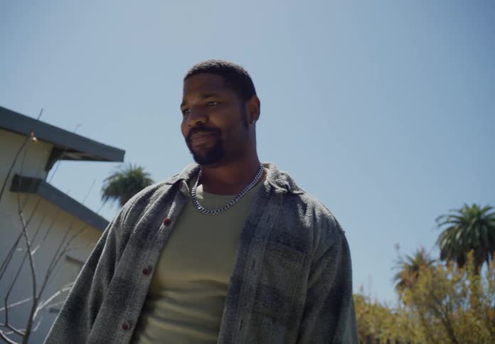 A man walking up to someone outside and talking to them near the house in the yard