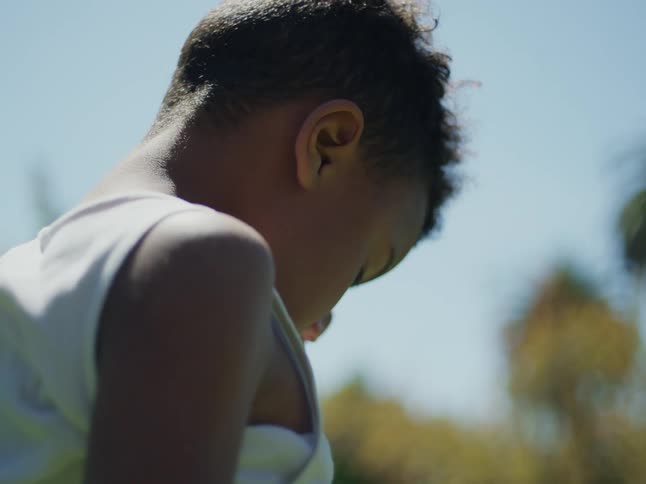 Back of a child rubbing his eyes on the backyard at daytime