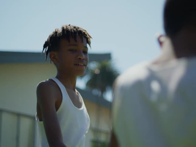 Boys with dreadlocks and white undershirts play with each other in the backyard on a sunny day